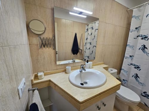 Modern bathroom with round sink, wooden vanity, illuminated mirror, and blue-patterned shower curtain at Olivia Playa La