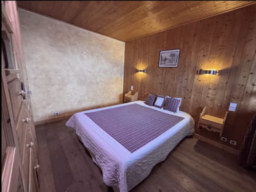Cozy wooden bedroom at Chez Francine with queen bed, plaid bedding, wall sconces, and mountain views from Notre Dame de