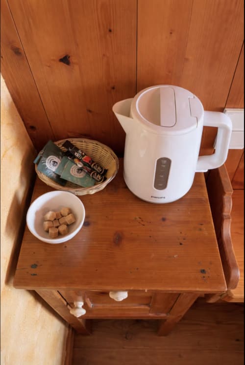 Welcome amenities on wooden table: electric kettle, coffee packets, sugar cubes, and wicker basket in Chez Francine room