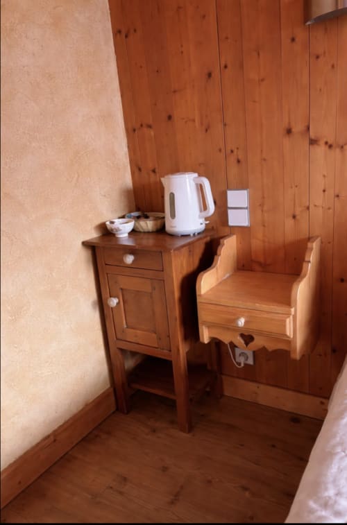 Rustic wooden bedroom corner at Chez Francine with electric kettle, nightstand, and chair in Notre Dame de Bellecombe