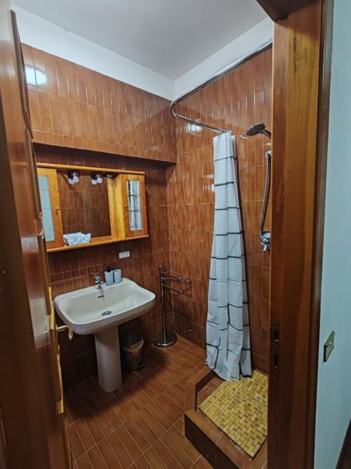 Modern bathroom at Villa Andreina with brown tiled walls, pedestal sink, shower with curtain, and wooden mirror cabinet in