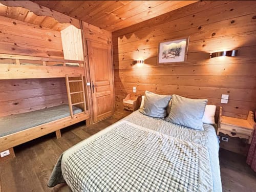Cozy wooden cabin bedroom at Chez Francine with queen bed, bunk beds, and rustic pine interior in Notre Dame de Bellecombe