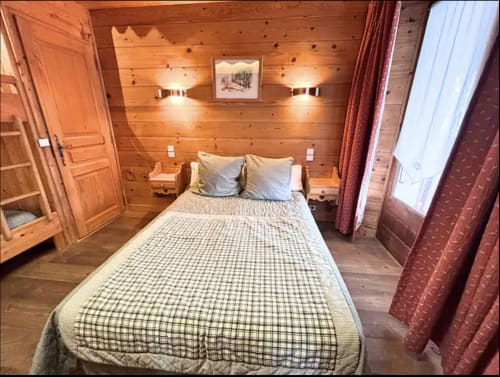 Cozy wooden bedroom at Chez Francine with queen bed, warm lighting, and rustic Alpine decor in Notre Dame de Bellecombe