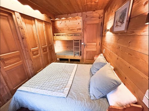Cozy wooden bedroom at Chez Francine with double bed, bunk beds, and rustic pine interior in Notre Dame de Bellecombe