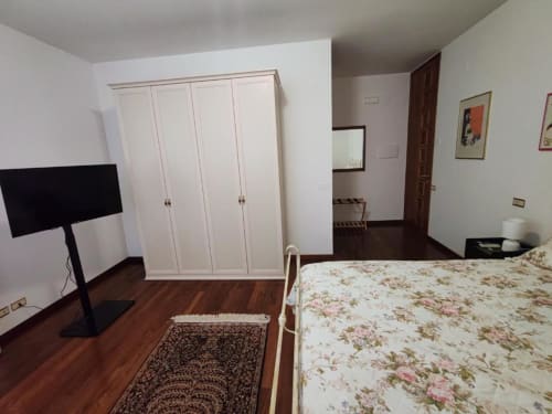Large double bedroom at Villa Andreina B&B in Sarnano with white wardrobe, floral bedding, wooden floors and TV