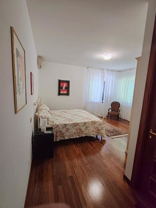 Large double bedroom at Villa Andreina with mountain views, wooden floors, bed, chair, and windows with sheer curtains