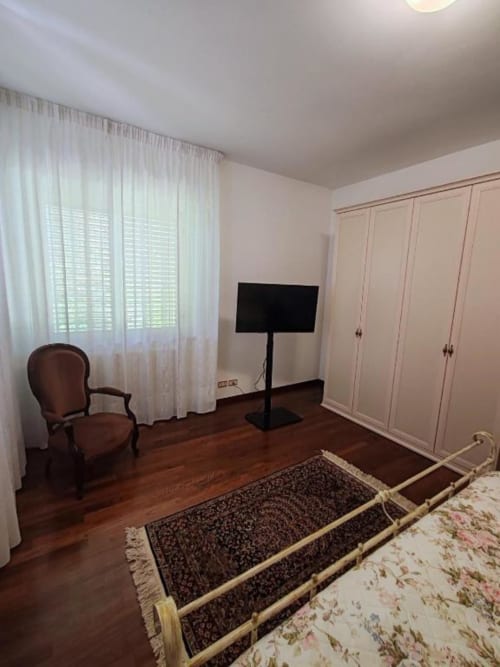 Spacious bedroom at Villa Andreina in Sarnano with wooden floors, TV stand, wardrobe, and mountain views from large windows