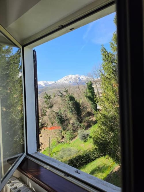 Open window at Villa Andreina in Sarnano showing snow-capped mountain, lush green landscape and cypress trees
