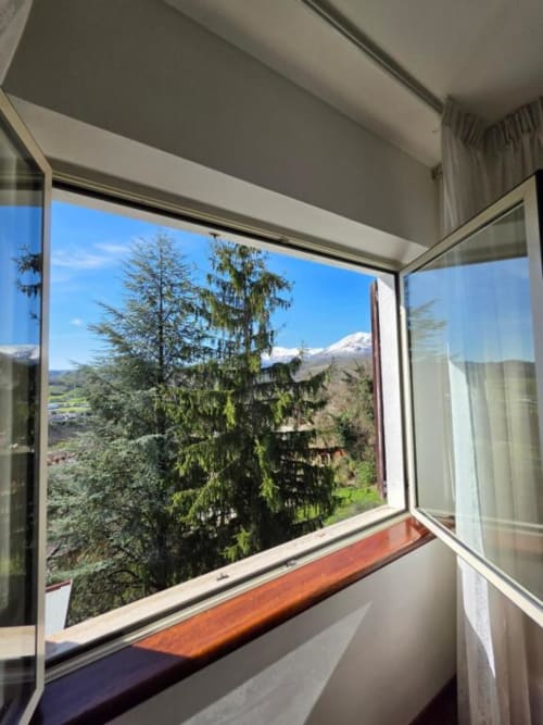 Mountain view from Villa Andreina room window overlooking snow-capped peaks and forest in Sarnano