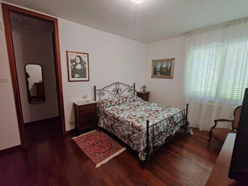 Bedroom at Villa Andreina in Sarnano with wrought iron bed, floral bedding, dark wood floors and garden view windows
