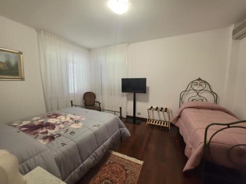 Villa Andreina double room with extra bed in Sarnano, featuring two beds, TV, and garden view with white curtains