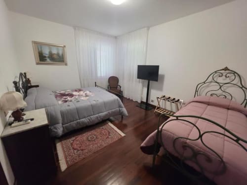 Double bedroom with extra bed at Villa Andreina in Sarnano, featuring wrought iron beds, TV, and garden views