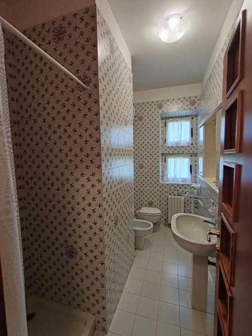 Villa Andreina bathroom in Sarnano with patterned wallpaper, toilet, sink, shower, and windows with garden view