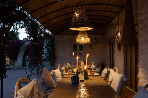 Candlelit dining terrace at Domaine Belhazar, Essaouira with woven pendant light and cushioned chairs overlooking courtyard