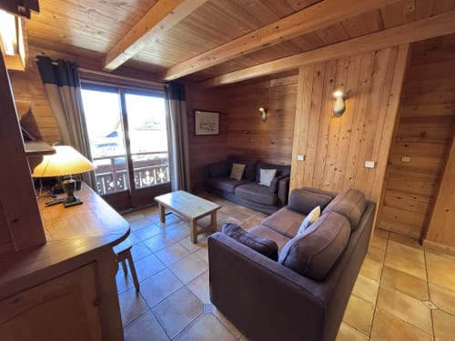 Spacious wooden mountain apartment living room with gray sofas, mountain view balcony, and modern amenities in Notre Dame de