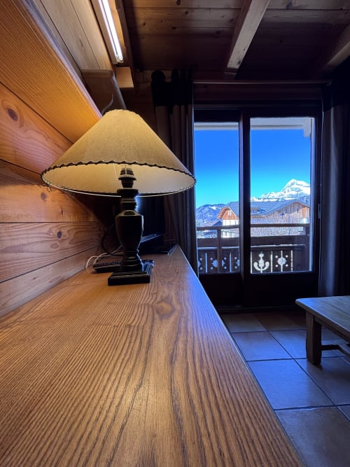 Cozy wooden apartment interior with black table lamp and snow-capped mountain views through glass doors, Notre Dame de