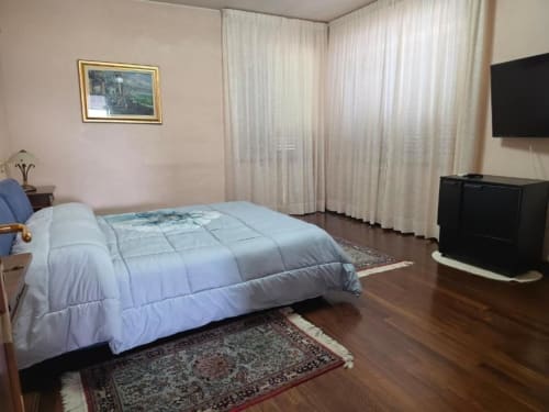 Villa Andreina Suite Room No.1 in Sarnano with blue comforter, flat-screen TV, and garden views from sheer curtains
