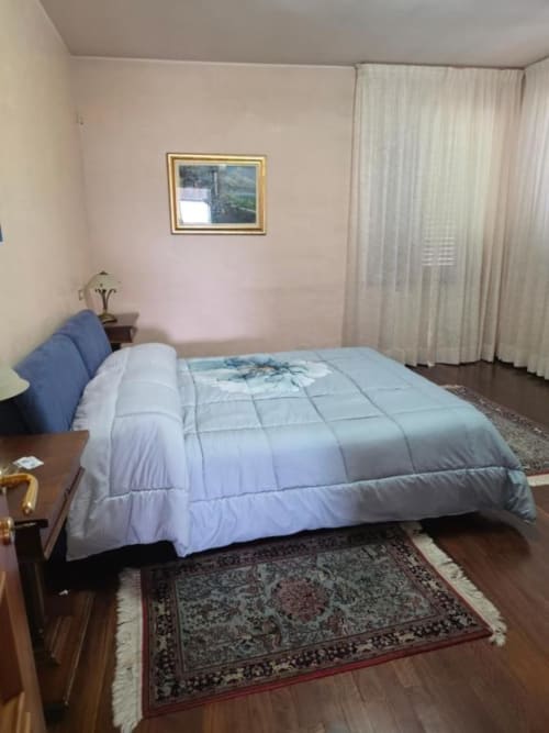 Spacious bedroom at Villa Andreina B&B in Sarnano with queen bed, blue pillows, and garden view through sheer curtains