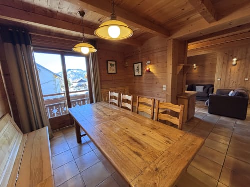 Spacious wooden alpine apartment dining area with mountain views, wooden table, pendant lights, and living room access at