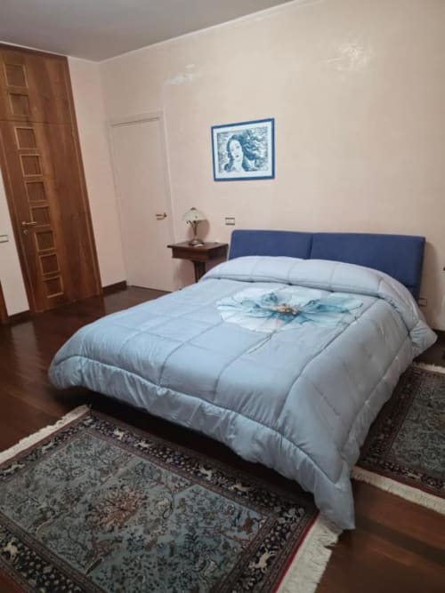 Blue upholstered bed with light bedding in Villa Andreina suite room in Sarnano, featuring wooden doors and framed artwork
