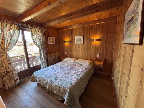 Cozy wooden bedroom at Chez Francine with double bed, mountain view balcony, and traditional Alpine decor in Notre Dame de