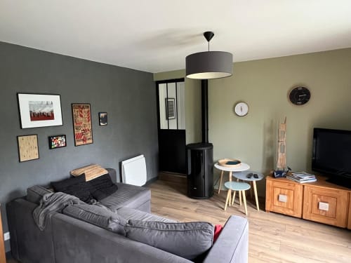Salon moderne à Destination Etretat avec canapé gris, luminaire suspendu, meubles en bois et galerie murale