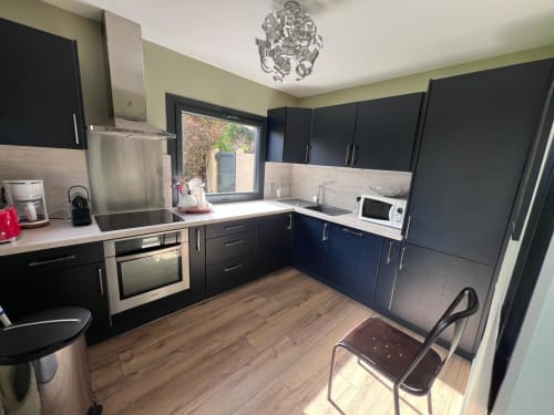 Cuisine moderne noire avec électroménagers en acier inoxydable, parquet clair et dosseret crème à l'hôtel Destination Etretat