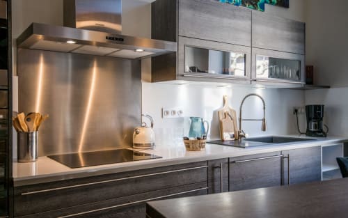 Cuisine moderne de l'appartement de Millau avec dosseret en acier inoxydable, plans de travail blancs et armoires en bois foncé