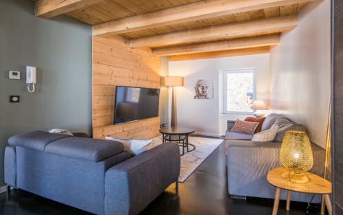 Séjour moderne de duplex à Millau avec poutres apparentes, canapés bleus, TV murale et éclairage chaleureux