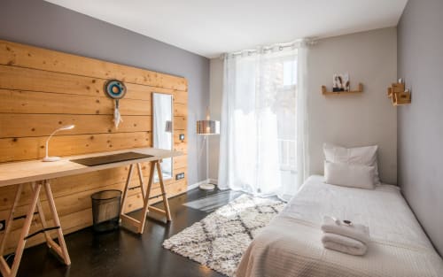 Chambre de studio moderne à Millau avec mur d'accent en bois, bureau, lit et vue sur la ville depuis les grandes fenêtres