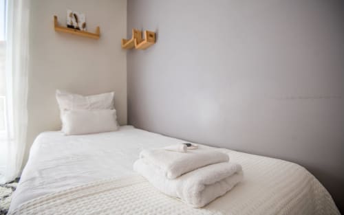 Chambre épurée à La Conciergerie Millau avec literie blanche, serviettes empilées et étagères murales en bois