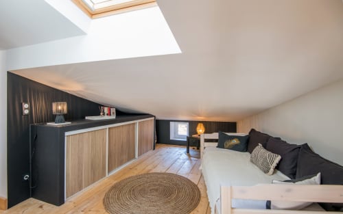 Chambre de loft duplex moderne à Millau avec puits de lumière, mobilier noir, parquet, canapé aux coussins noirs et vue sur la ville