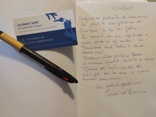 Biglietto da visita Co-Host Now e lettera scritta a mano con penna su superficie bianca, gestione proprietà Campagnano di Roma