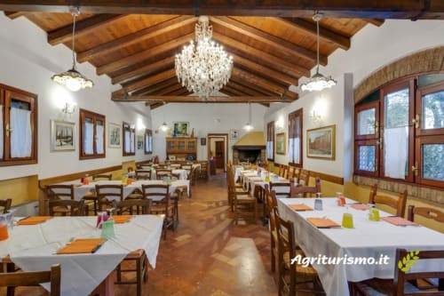 Sala da pranzo dell'Agriturismo Villa Mocenigo a Mirano con travi in legno, lampadari e tavoli apparecchiati