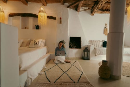 La Suite Beldi at Riad Eucalyptus in El Ghazouane: woman working on laptop in spacious room with built-in beds, wooden beams,