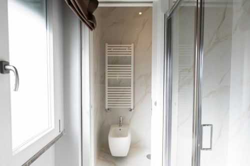 Bagno moderno alle Michelangelo Central Suites Firenze con pareti in marmo, lavandino bianco, scaldasalviette e box doccia