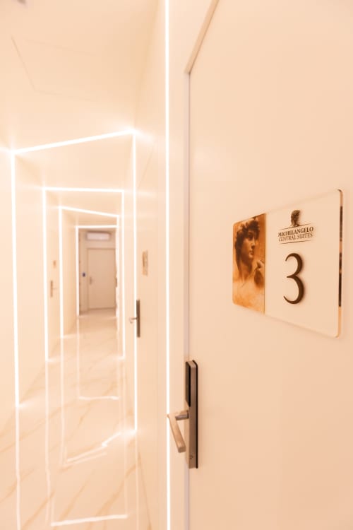 Corridoio moderno dell'hotel Michelangelo Central Suites a Firenze con porte in vetro illuminate al neon e cartello Stanza 3