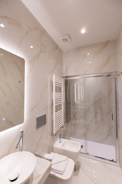 Lussuoso bagno nelle Michelangelo Central Suites Firenze con pareti in marmo, doccia in vetro, specchio illuminato e arredamento moderno