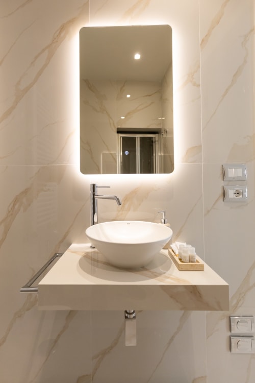 Bagno moderno nelle Michelangelo Central Suites Firenze con lavabo bianco a bacinella, specchio LED e pareti in marmo