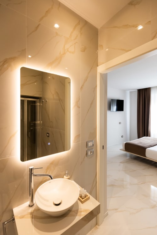 Bagno moderno della camera Queen Superior presso Michelangelo Central Suites, Firenze con specchio illuminato e pareti in marmo