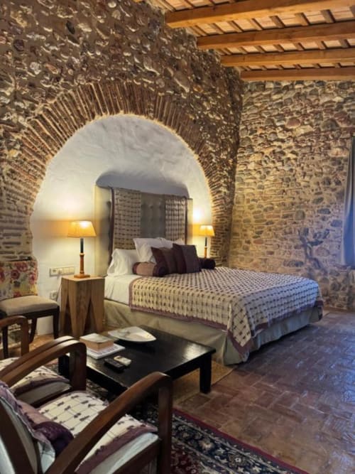 Dormitorio rústico de piedra en Hotel Can Carbó de les Olives con cama en alcoba abovedada, vigas vistas e iluminación cálida en Perelada