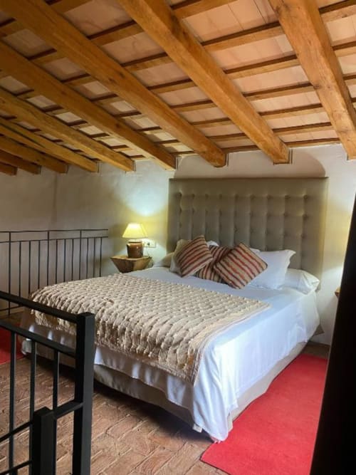 Habitación doble en Hotel Can Carbó de les Olives, Perelada, con vigas de madera, cabecero beige, almohadas a rayas y camino rojo