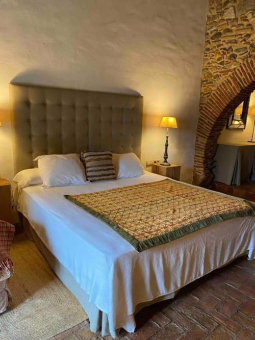 Habitación doble con cabecero tapizado, sábanas blancas, colcha decorativa e iluminación cálida en Hotel Can Carbó de les