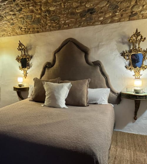 Dormitorio elegante en Hotel Can Carbó de les Olives en Perelada con cabecero ornamentado y espejos con marco dorado