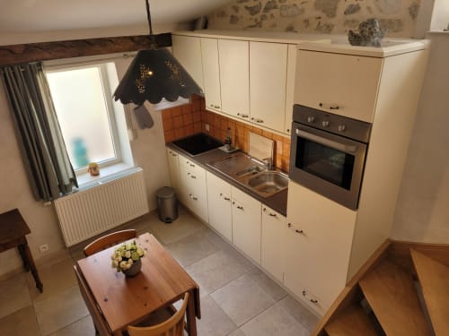Cuisine moderne équipée avec armoires crème, carrelage orange, cuisinière et évier en inox, table à manger fleurie au Gîte