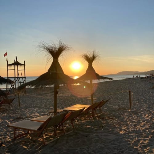 Spiaggia al tramonto presso Agriturismo La Tortorella di Grosseto con ombrelloni in paglia e lettini