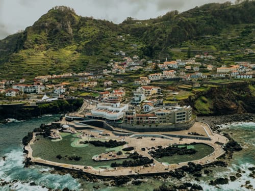 Hôtel de villégiature côtier perché sur une presqu'île rocheuse avec un village aux terrasses verdoyantes en arrière-plan à Funchal, Portugal