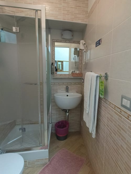 Bagno moderno dell'Hotel Principe Amedeo Roma con doccia, lavabo rotondo, specchio, scaldarancia e pavimentazione effetto legno