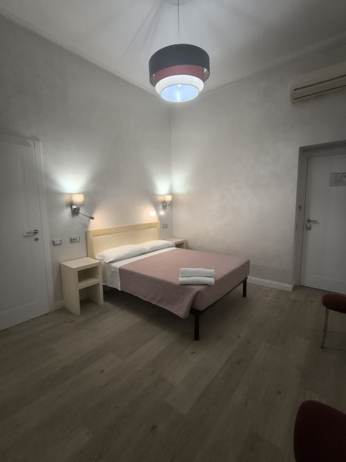 Moderna camera d'hotel presso l'Hotel Principe Amedeo Roma con letto queen, muri bianchi, illuminazione a soffitto e pavimento in legno