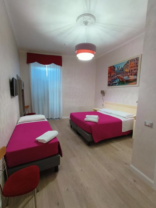 Luminosa camera tripla all'Hotel Principe Amedeo Roma con tre letti, lampada a sospensione e quadri con vedute cittadine